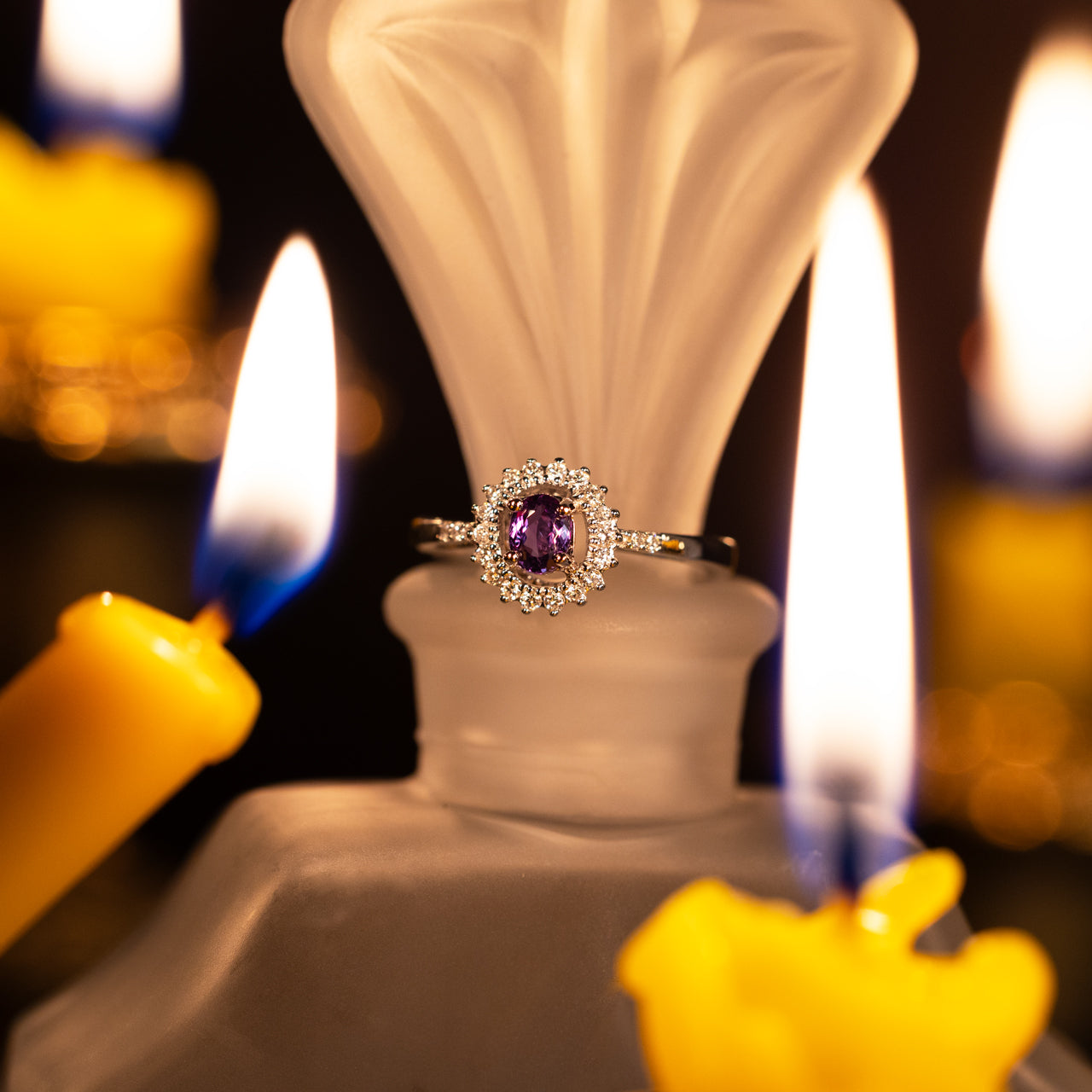 Natural alexandrite and diamond halo ring in 18k white gold with a purple center stone surrounded by sparkling diamonds, illuminated by candlelight.
