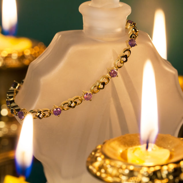 Detail of the 3.00ctw natural alexandrite 18k yellow gold bracelet with its vibrant purple stones resting on a candle for an atmospheric display
