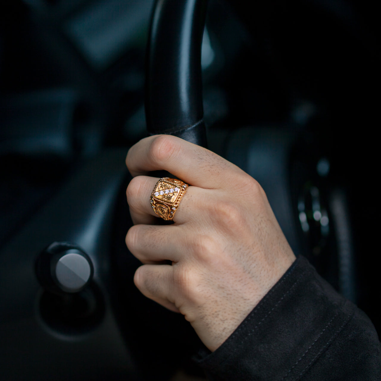 Men's 0.61ctw diamond 18k yellow gold ornate signet ring on hand holding steering wheel