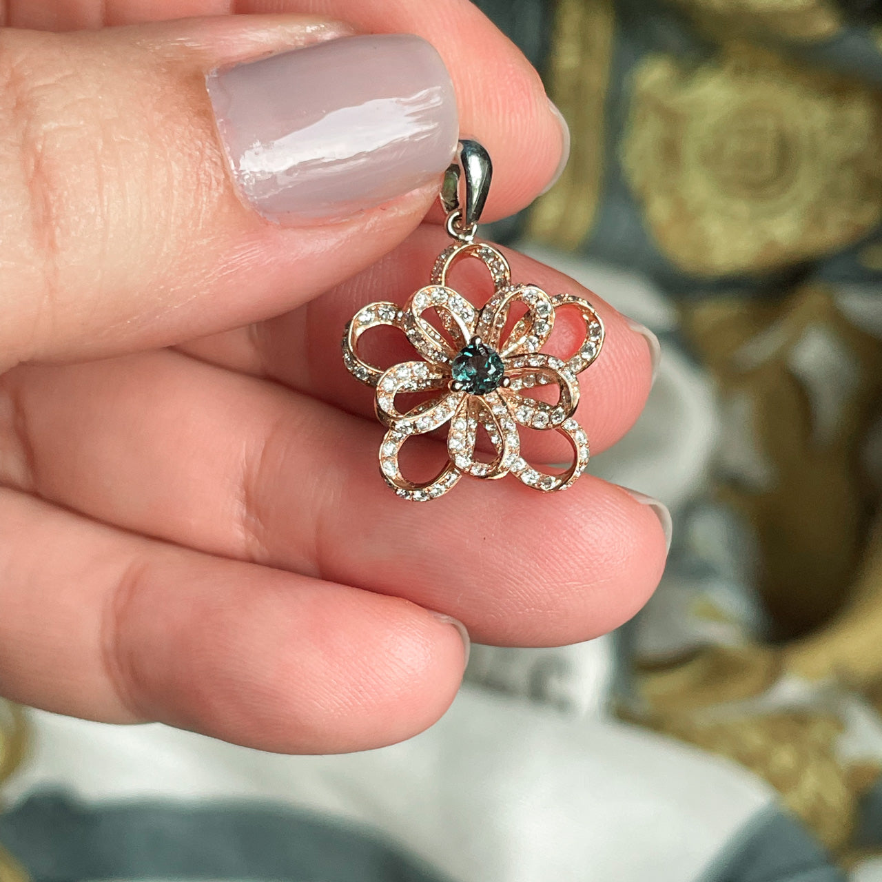 A person's hand presenting the 0.18ct natural alexandrite flower pendant in 18k multitone gold