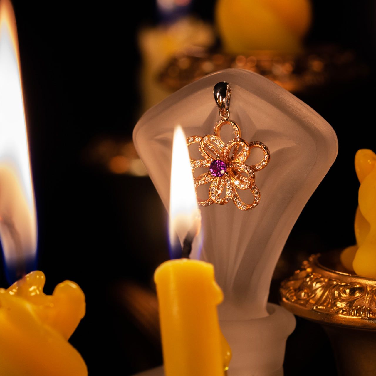18k multitone gold flower pendant with natural alexandrite center and diamond accents displayed on frosted stand surrounded by candlelight