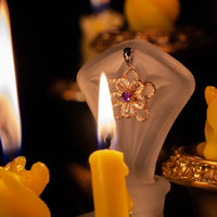 Thumbnail for 18k multitone gold flower pendant with natural alexandrite center and diamond accents displayed on frosted stand surrounded by candlelight