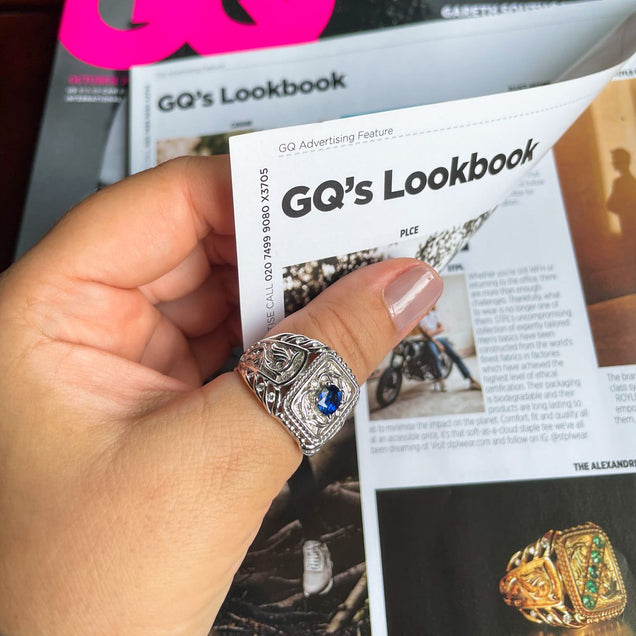 Individual presenting a men's signet ring alongside a magazine, showcasing the 0.80ct blue sapphire and 18k white gold design
