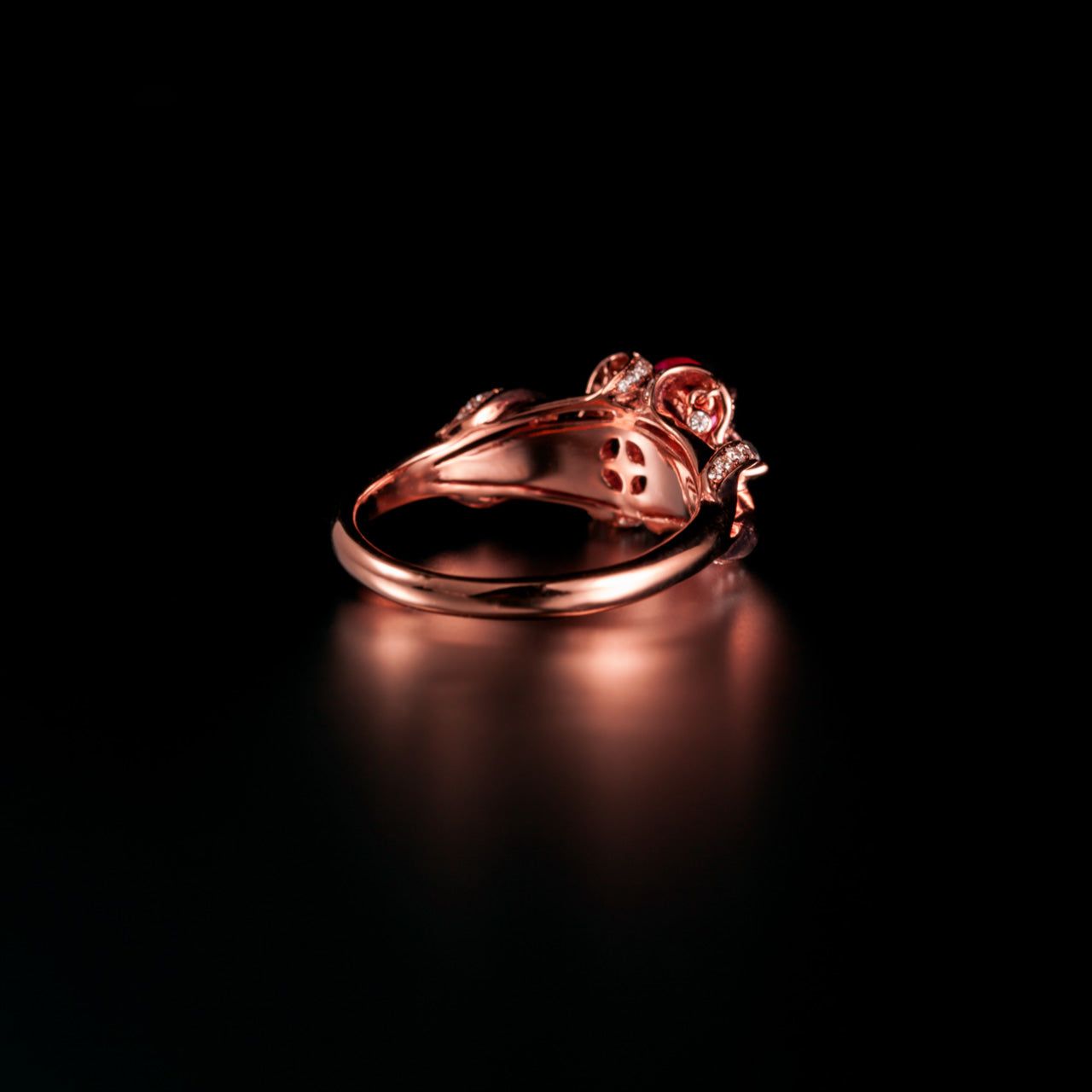 18k rose gold ring with natural pear-shaped ruby, round alexandrites, and channel-set diamonds on black background