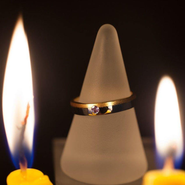 Romantic setting with a two-toned 18k gold wedding band with natural alexandrite beside lit candles