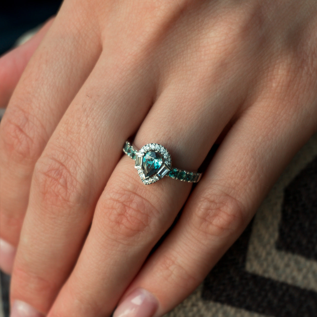 A woman's hand displaying a platinum ring with a 0.57ct alexandrite that appears blue under certain lighting