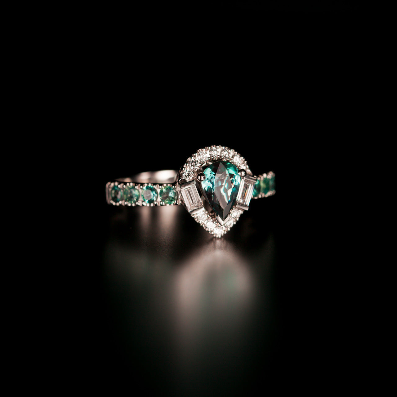 Natural alexandrite platinum ring with pear-shaped center stone, diamond halo, and accent alexandrite gemstones.