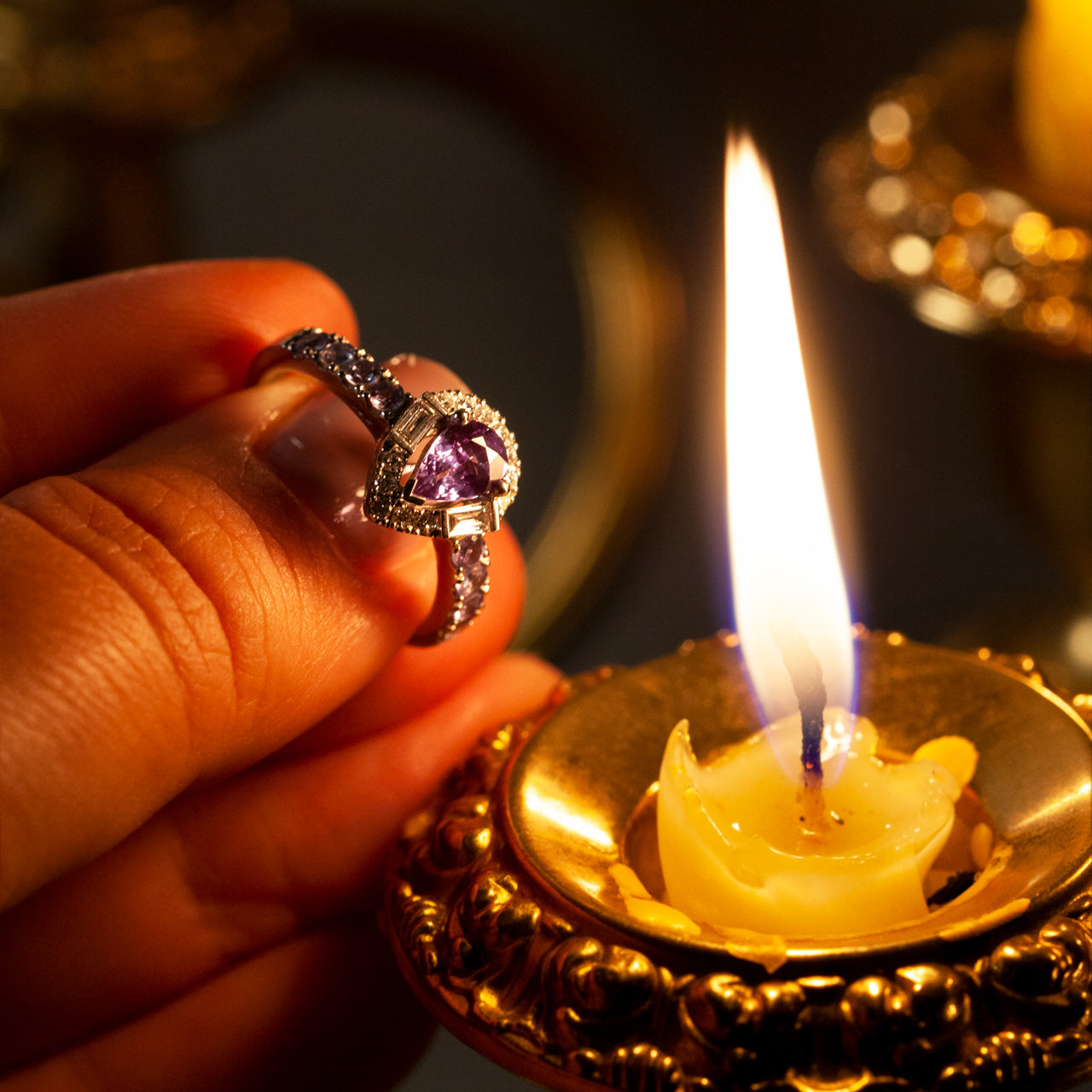 A woman's hand elegantly holding a platinum ring with a 0.57ct alexandrite in front of a soft candle glow