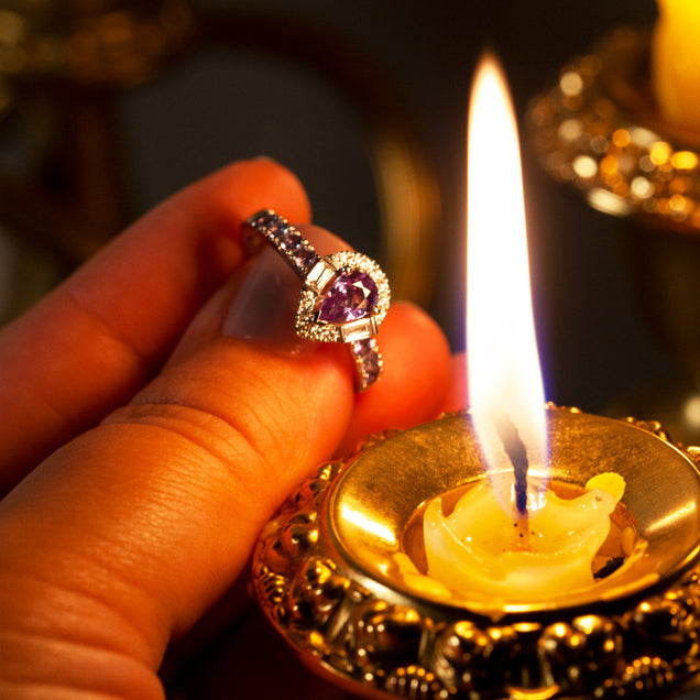 A woman's hand elegantly holding a platinum ring with a 0.57ct alexandrite in front of a soft candle glow