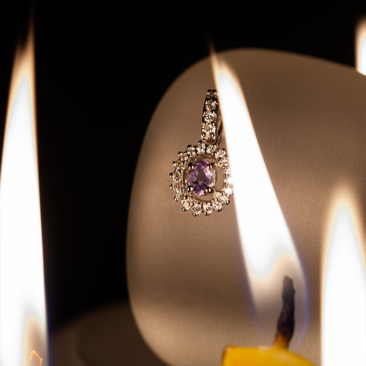 18k white gold pendant with a 0.27ct natural Alexandrite stone displayed on a candle