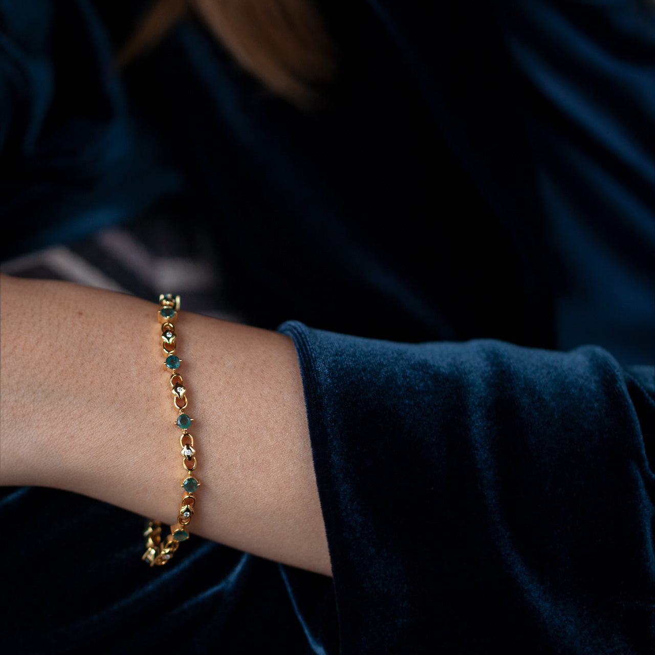 A woman's wrist adorned with the luxurious 3.00ctw natural alexandrite 18k yellow gold bracelet, complemented by her blue velvet attire