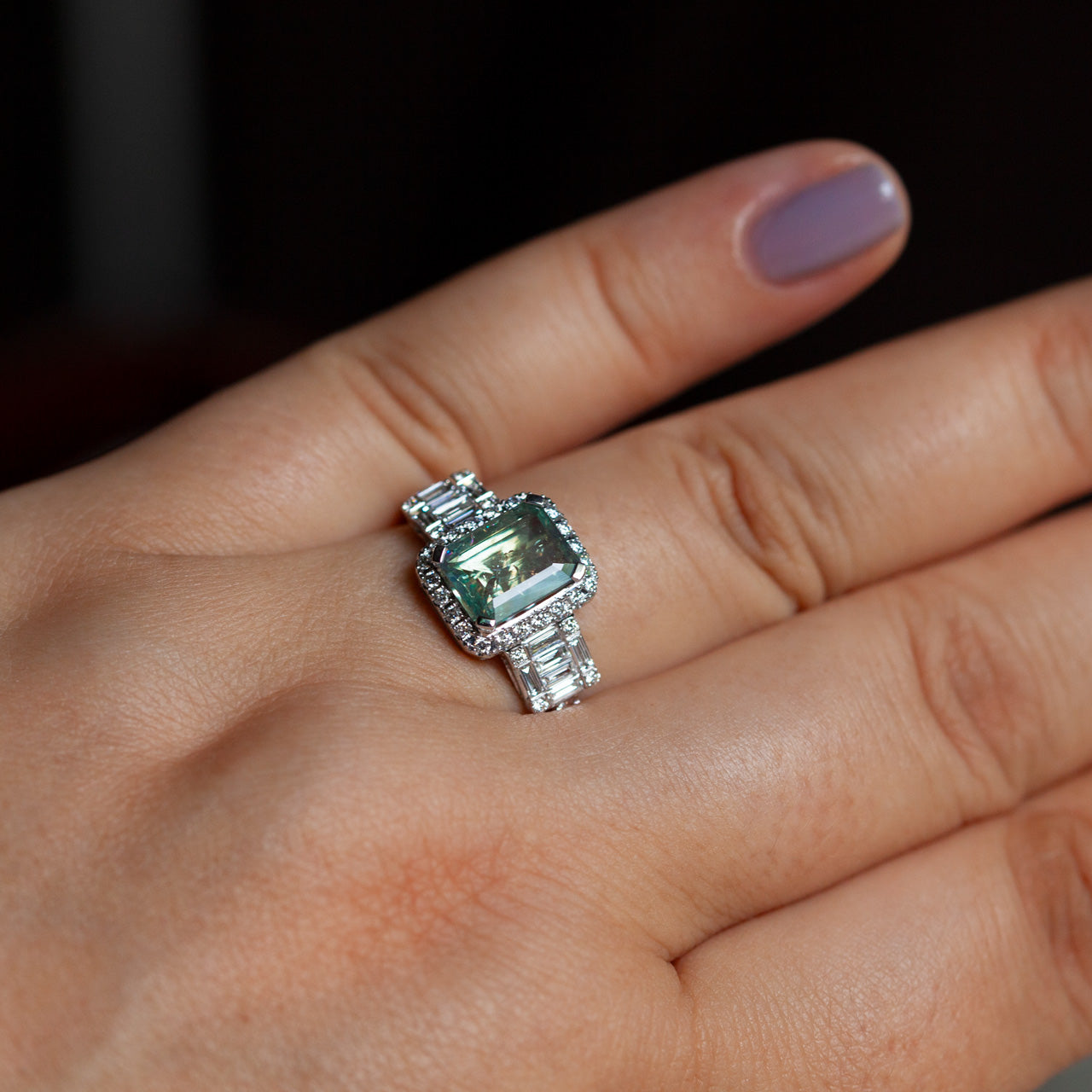 A woman's hand presenting a luxurious 18k white gold ring with a color-changing alexandrite stone