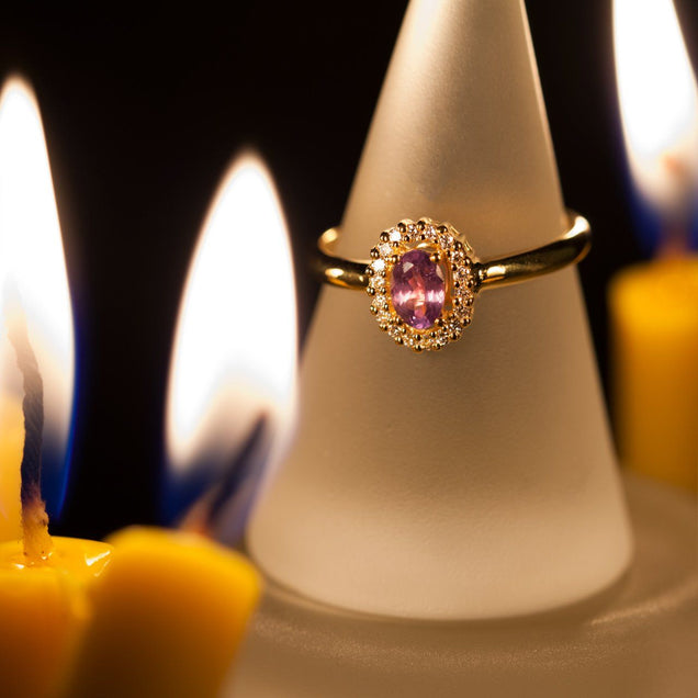 Close-up of a 0.55ct natural alexandrite ring on a candle, emphasizing the gemstone's pink to green color change in 18k yellow gold setting
