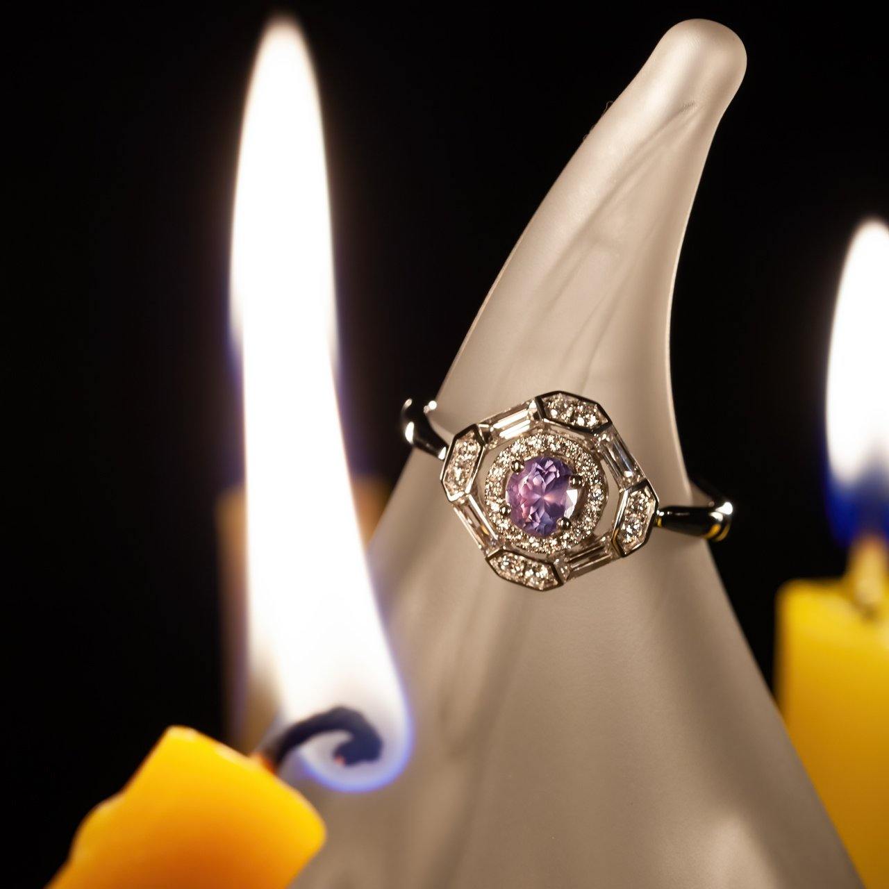 Close-up of a natural alexandrite ring with diamonds set in platinum, shown glowing near candlelight highlighting its color-change feature