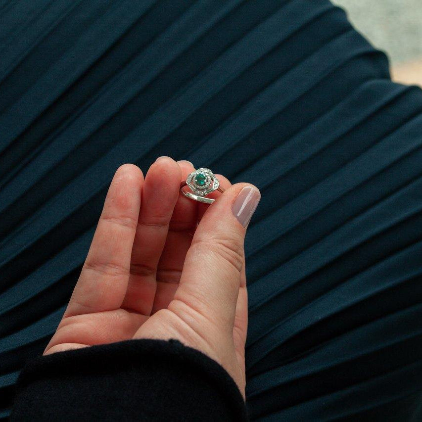 Close-up of 0.45ct natural alexandrite ring with diamonds in platinum setting held by hand against dark pleated fabric background