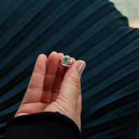 Thumbnail for Close-up of 0.45ct natural alexandrite ring with diamonds in platinum setting held by hand against dark pleated fabric background