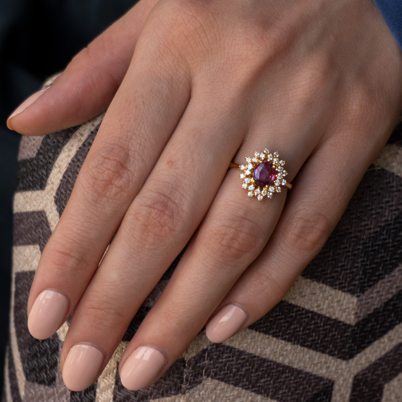 A woman's hand displaying a 1.28ct pink sapphire ring in an 18k yellow gold setting