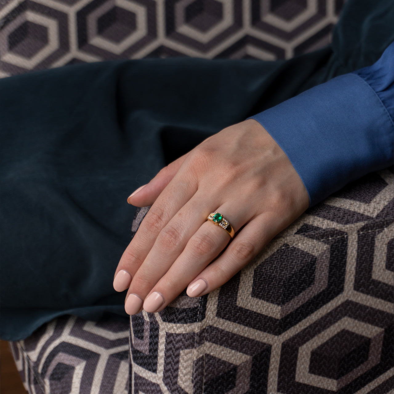 Woman's hand displaying a 0.64ct natural emerald ring in 18k yellow gold on a couch
